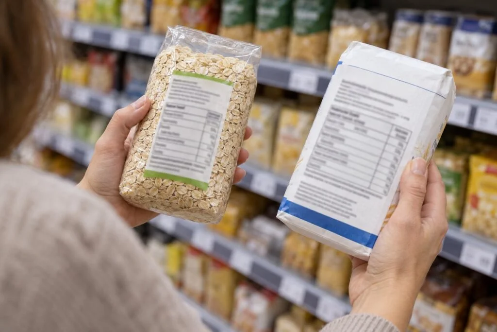 Osoba w sklepie porównuje etykiety dwóch produktów spożywczych